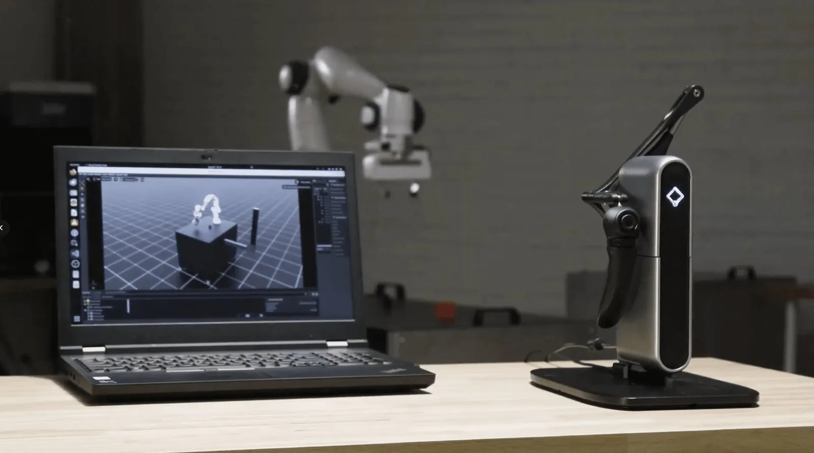 Inverse3 on a desk next to a laptop and a robot arm it controls